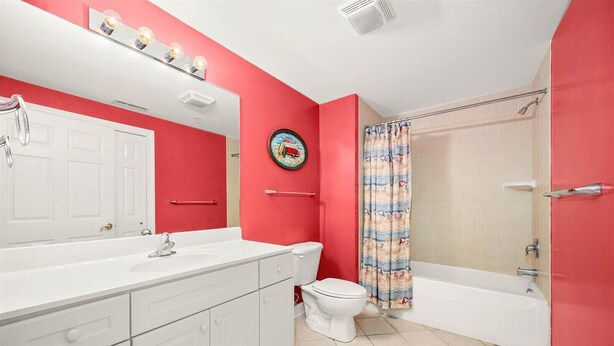 Un baño con tocador blanco, inodoro, ducha con cortina y pared de acento roja.