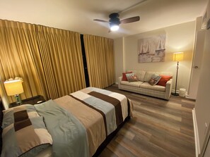 A hotel room with a bed, a sofa, a ceiling fan, and a painting on the wall.
