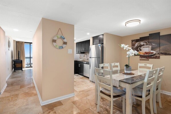 A modern kitchen with a refrigerator, stove, and dining area with chairs and a table. - Century One-2 Bedroom Ocean Oasis with Indoor Pool! (Ocean City)