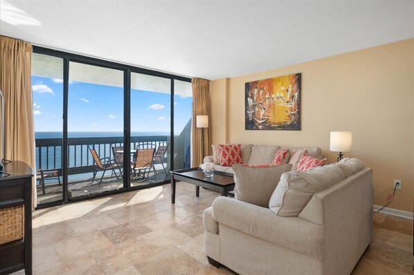 A living room with a large sliding glass door leading to a balcony with outdoor seating. - Century One-2 Bedroom Ocean Oasis with Indoor Pool! (Ocean City)