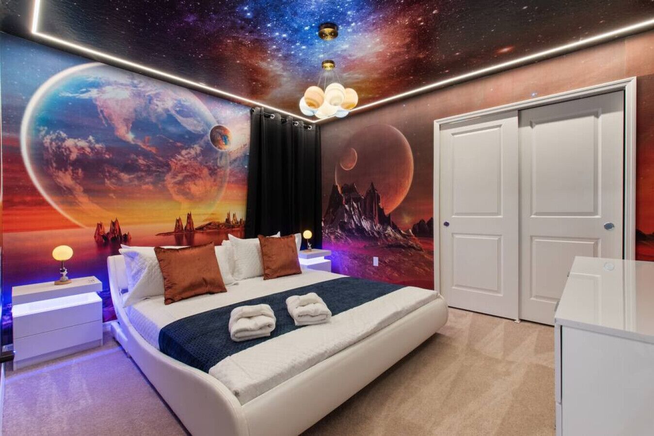 Ein Schlafzimmer mit einem Bett, einem Nachttisch, einer Kommode und einer Wandmalerei mit Weltraummotiven.