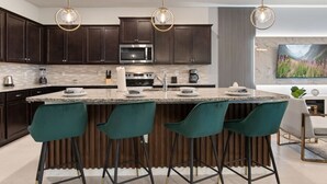 A modern kitchen with dark wood cabinets, a central island with bar stools, stainless steel appliances, and pendant lighting. - New Vacation Home Windsor Island by Disney w/Pool (Davenport)