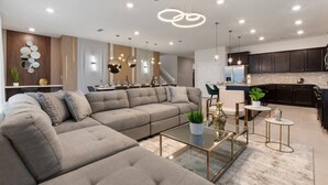 A modern living room with a sectional sofa, a glass coffee table, and pendant lighting. - New Vacation Home Windsor Island by Disney w/Pool (Davenport)