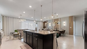 A modern kitchen with a central island, pendant lighting, and a dining area with chairs. - New Vacation Home Windsor Island by Disney w/Pool (Davenport)