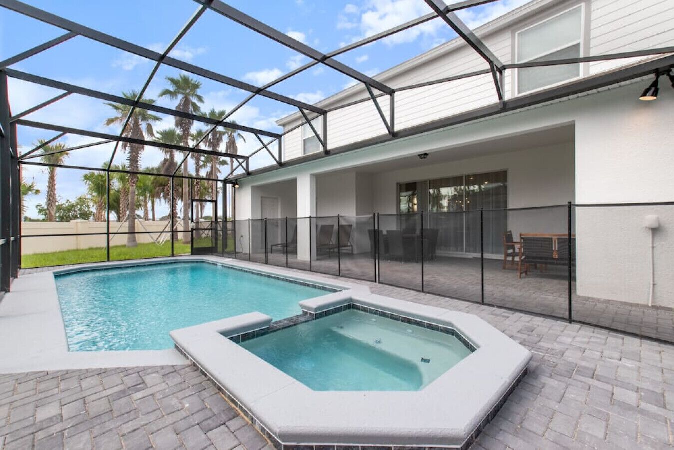 Une piscine avec un jacuzzi, entourée d’une terrasse couverte comprenant des chaises et une table.