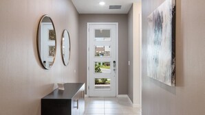 Un couloir avec une porte, deux miroirs, un comptoir noir et un tableau accroché au mur.