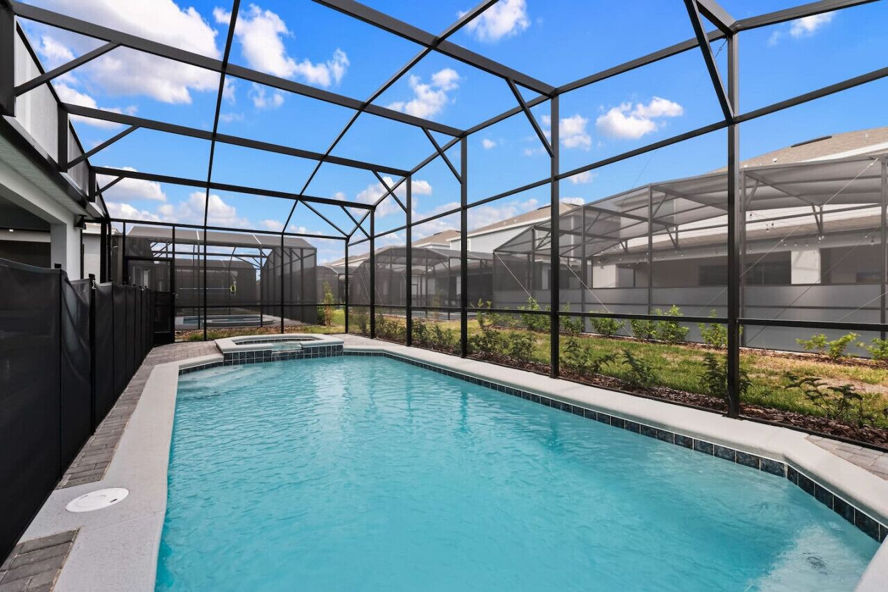 A swimming pool with a glass enclosure, surrounded by a metal frame and a grassy area.