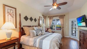 A bedroom with a bed, a nightstand, a lamp, a ceiling fan, a TV, and a window with curtains. - Stunning Briarwood Lakefront Pool and Spa Home (Naples)