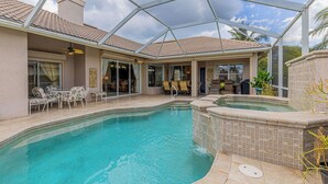 A swimming pool with a covered patio area, lounge chairs, and a hot tub. - Stunning Briarwood Lakefront Pool and Spa Home (Naples)