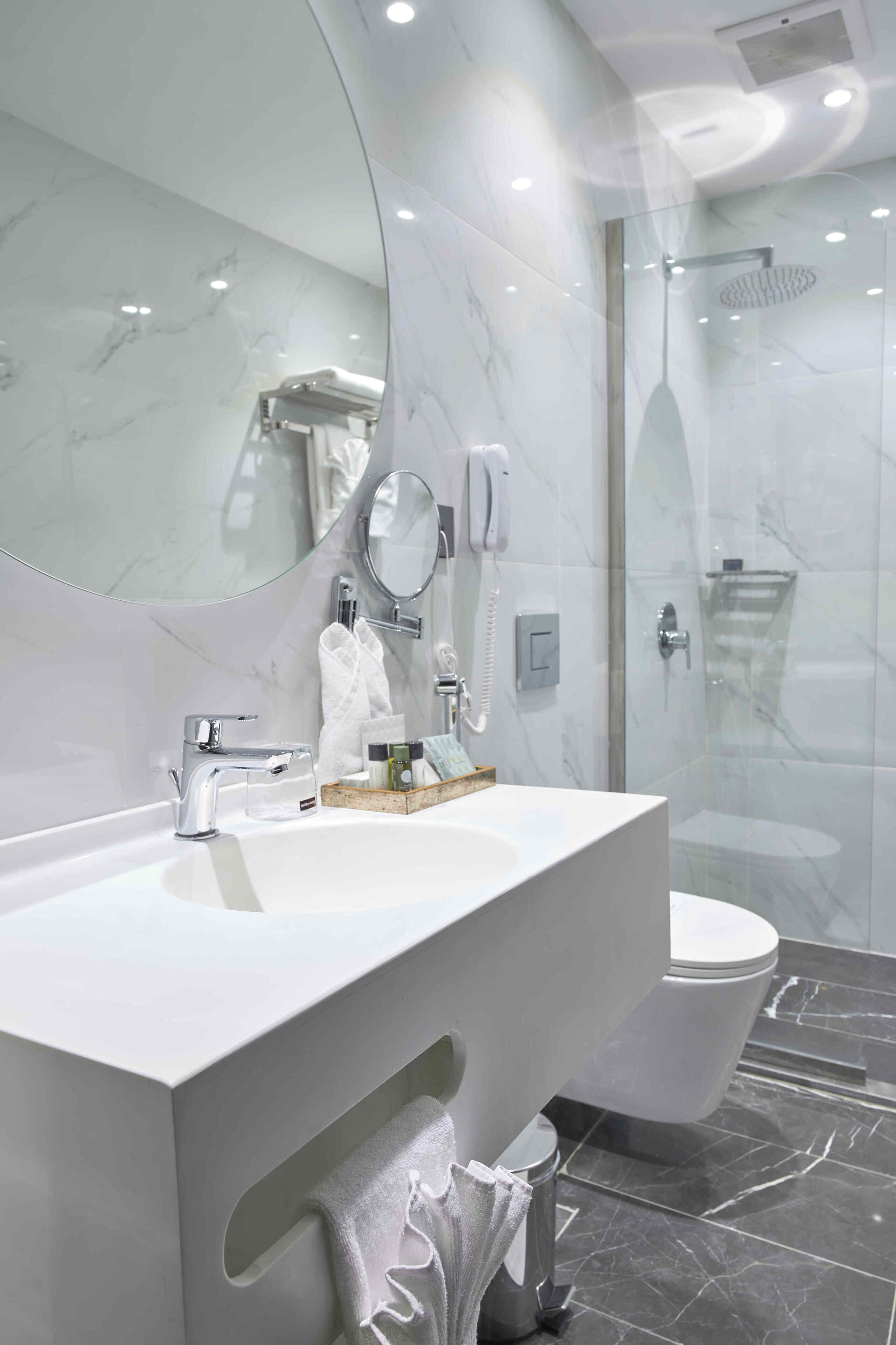 A modern bathroom with a white vanity, a large mirror, a glass-enclosed shower, and a toilet.