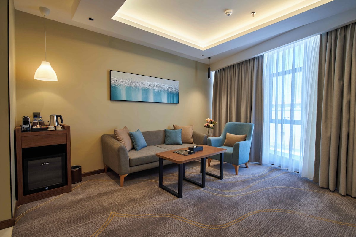 A modern hotel room with a sofa, armchair, coffee table, and a television.
