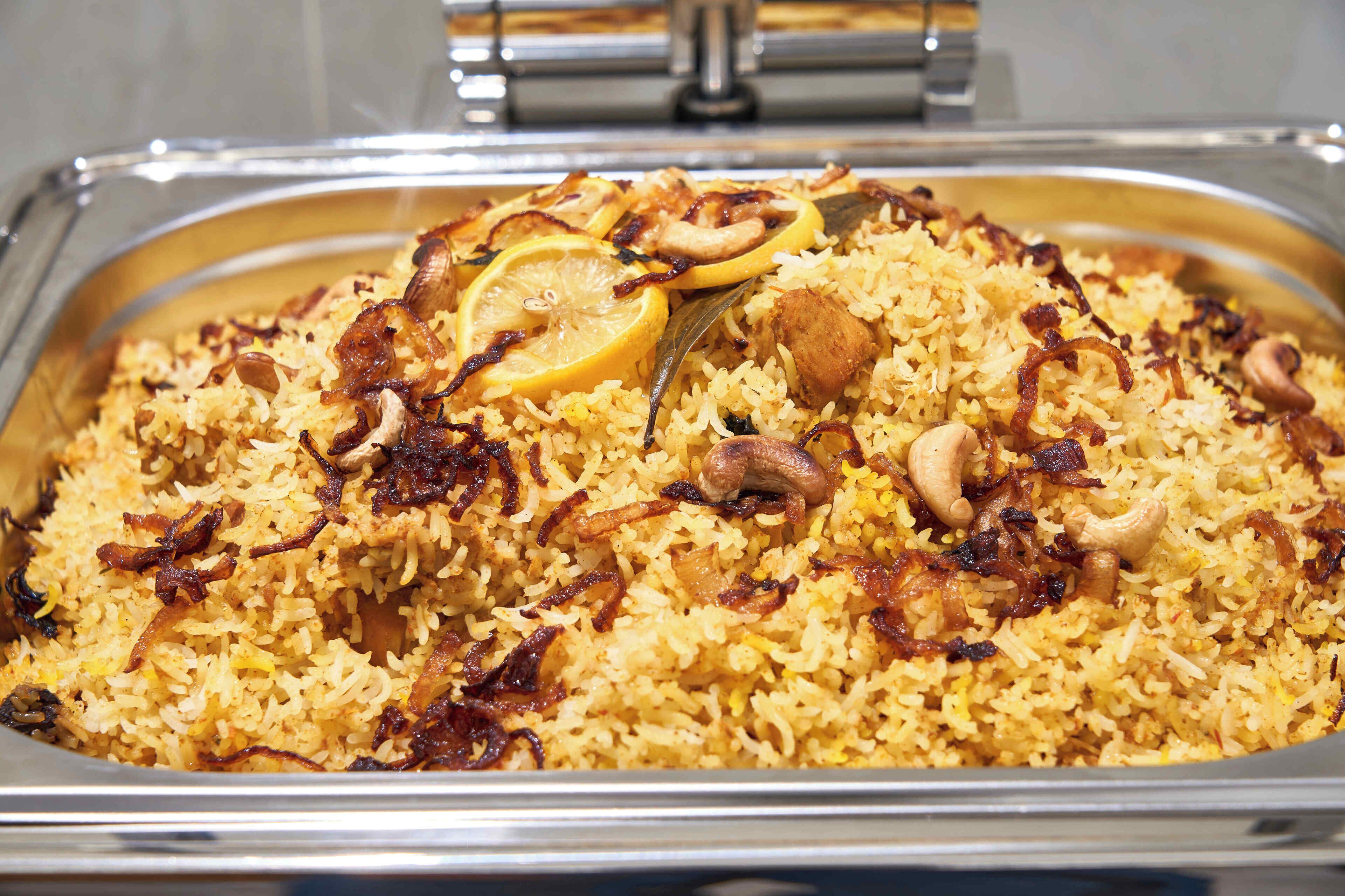 Un grand plat de service rempli de riz jaune, garni de tranches de citron, d’oignons frits et de noix.