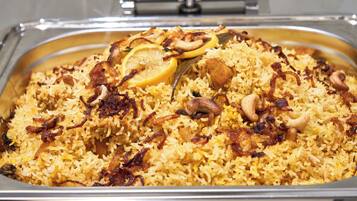 Un grand plat de service rempli de riz jaune, garni de tranches de citron, d’oignons frits et de noix.