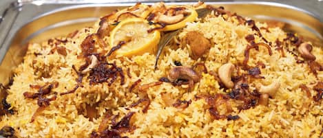 Un plato grande con arroz amarillo adornado con rodajas de limón, cebollas fritas y nueces.
