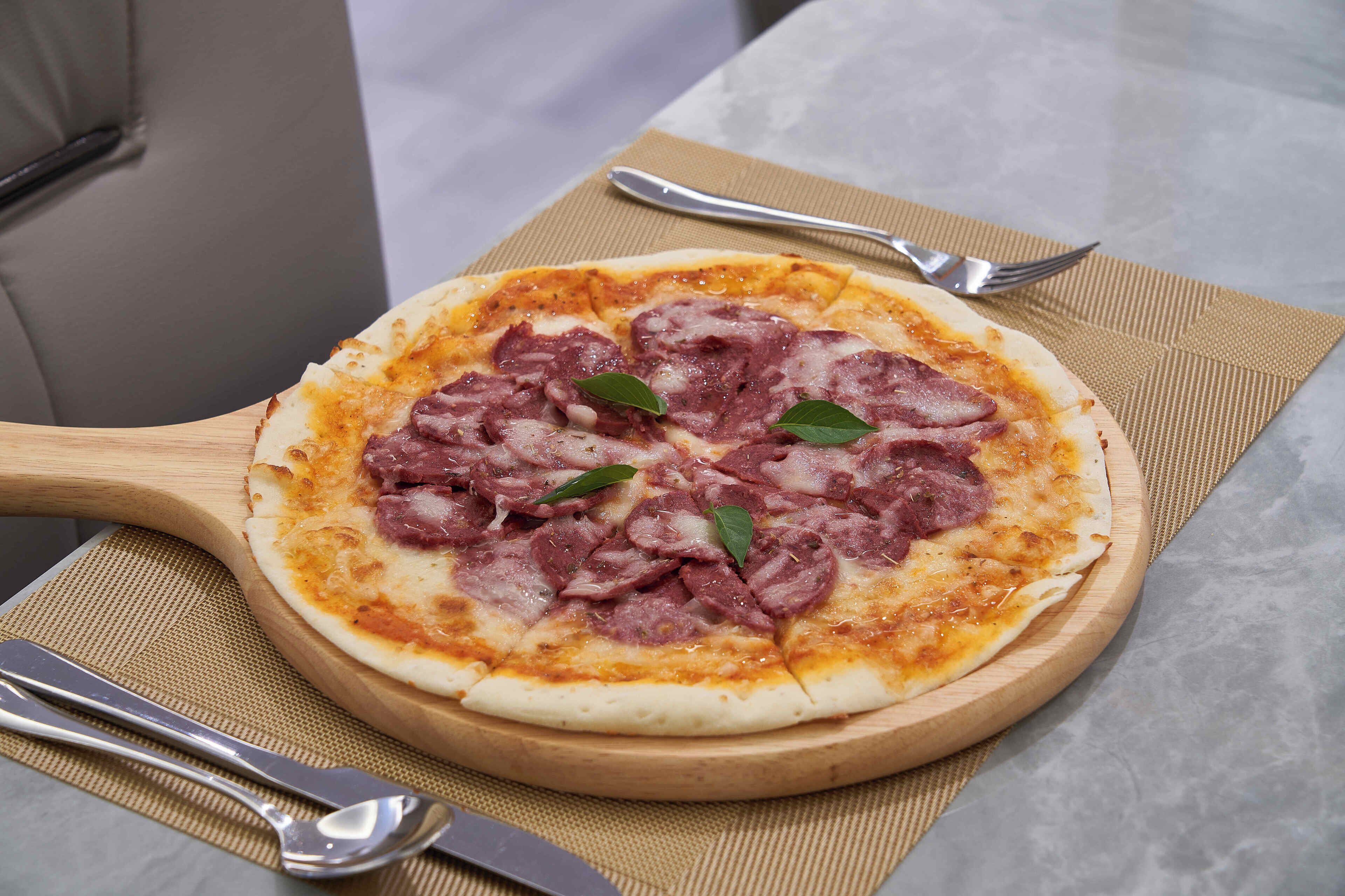Pizza op een houten plank met een mes en vork ernaast.