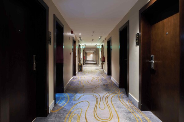 Un pasillo de hotel con alfombra estampada, puertas a ambos lados y señalización de salida de emergencia.