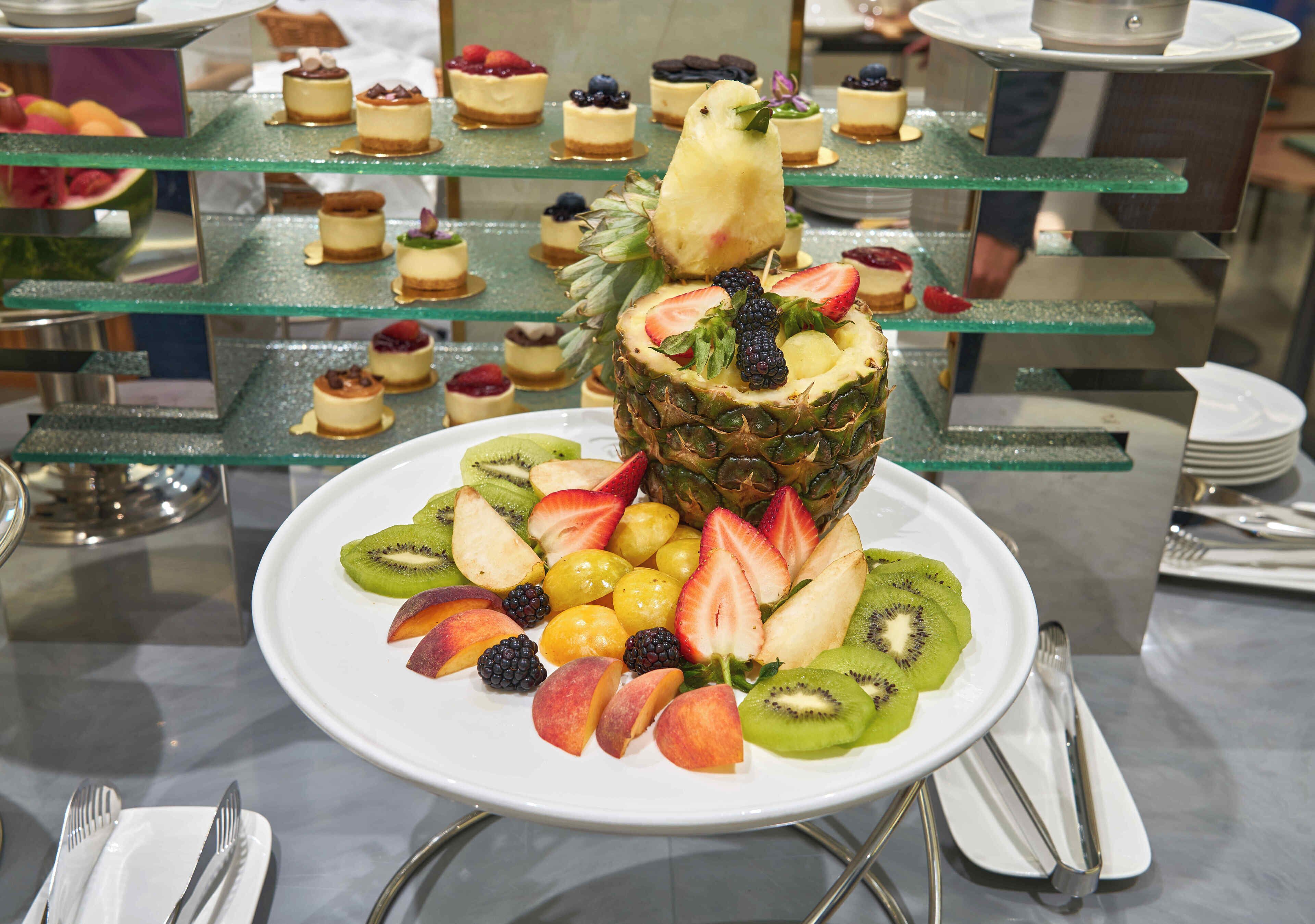 A fruit platter with a bird on top, surrounded by various desserts on glass stands.