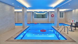 Una piscina interior moderna con agua cristalina azul, paredes de azulejos e iluminación empotrada en el techo.
