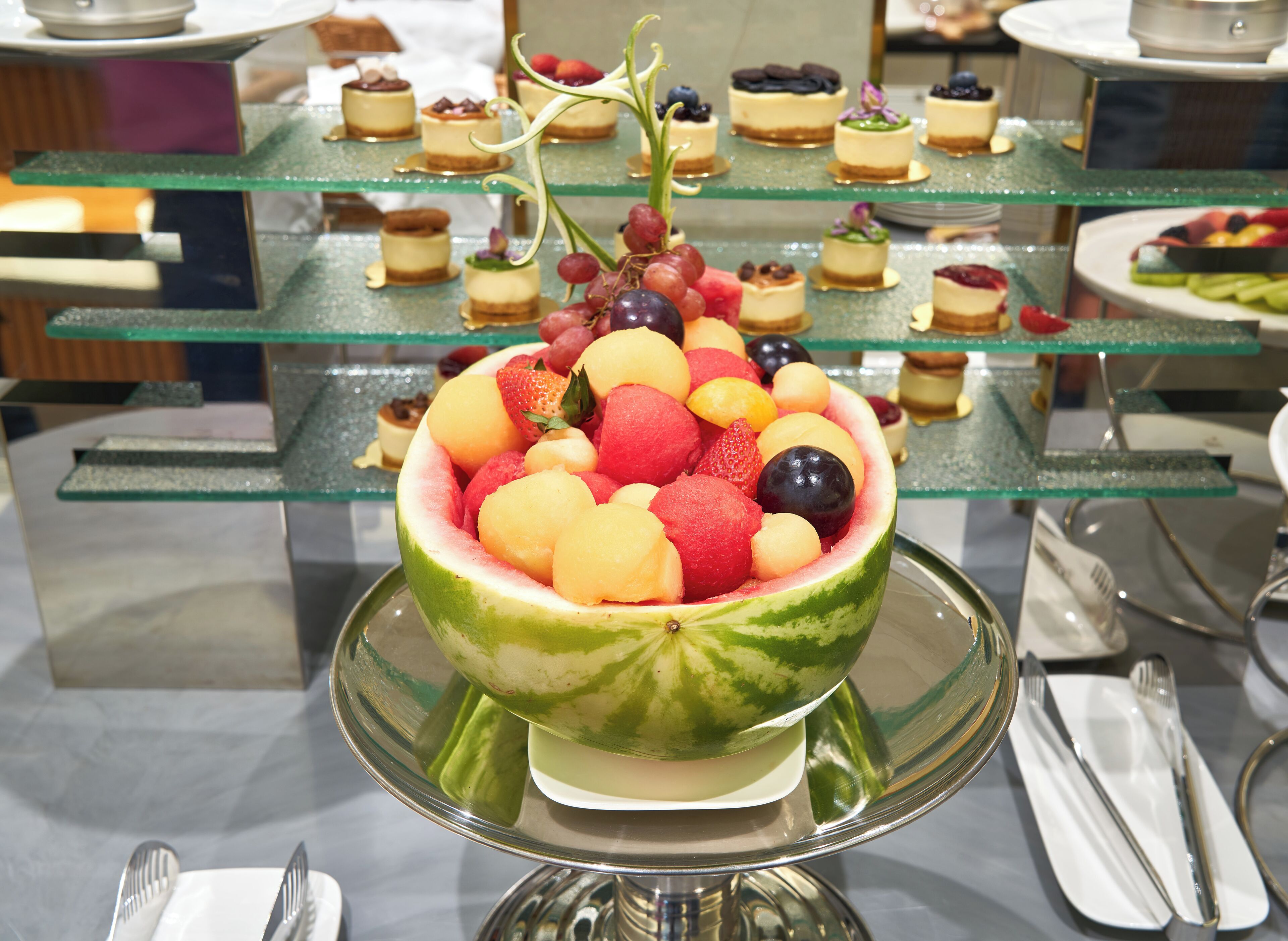 A fruit bowl filled with various fruits on a glass stand.