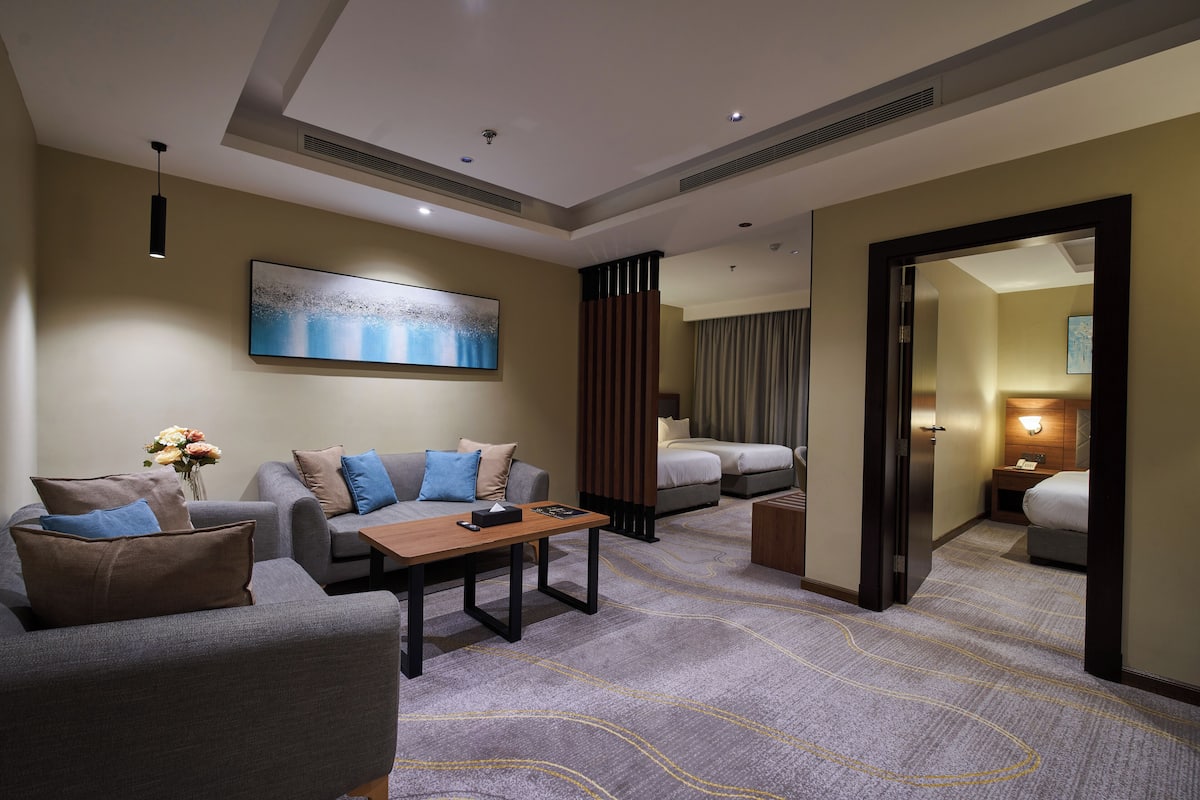 A hotel room with a sofa, a table, a bed, and a mirror.