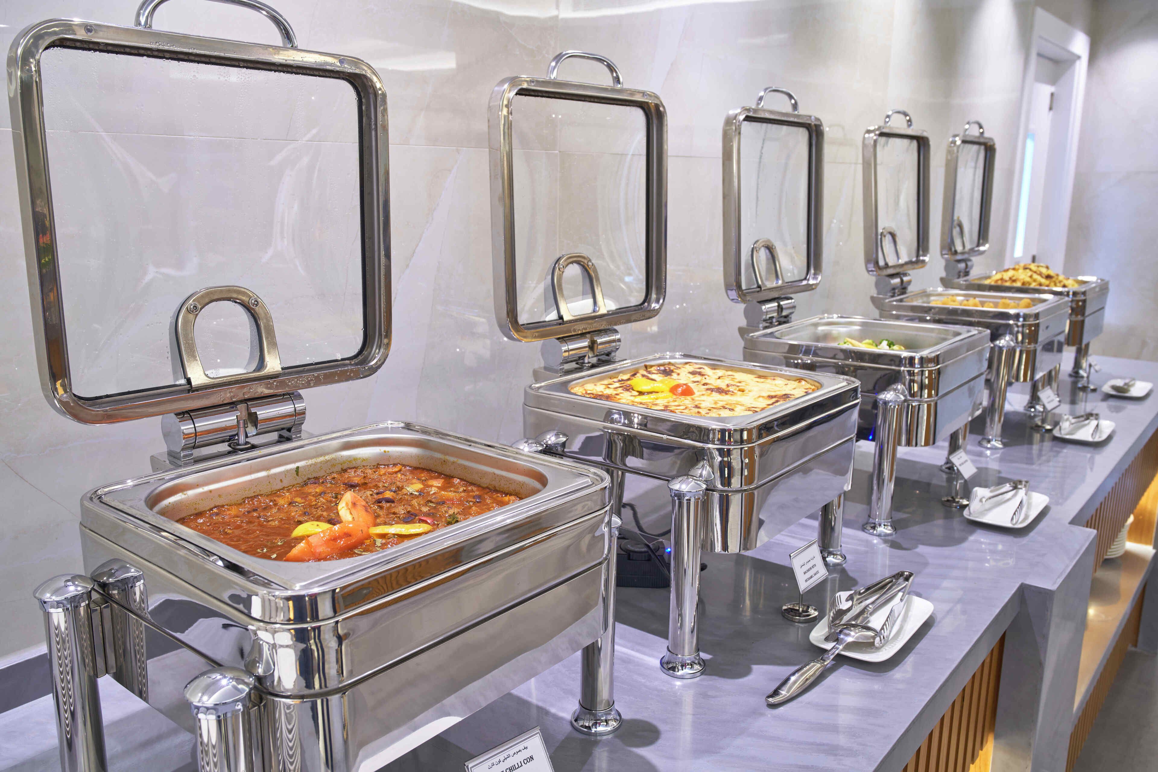 A buffet setup with multiple stainless steel chafing dishes, each with a handle, and a sign indicating the type of food.