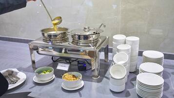 Montaje de bufé con varios recipientes de comida, platos apilados y un cartel que indica 'LENTIL SOUP'.