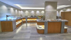 Un moderno vestíbulo de hotel con un mostrador de recepción central, varias zonas de estar y una mesa de buffet.