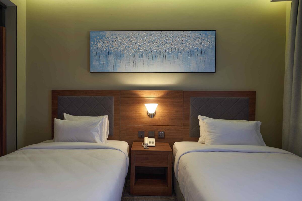 A hotel room with two beds, a nightstand with a phone, and a wall-mounted artwork.