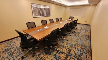 Uma sala de conferências com uma mesa comprida, cadeiras pretas, um projetor e piso coberto de carpete.