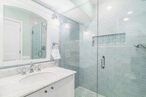 A bathroom with a glass shower enclosure, a white sink with a marble countertop, and a mirror with a white towel hanging on the wall. - Updated villa on golf course, 3 min to beach! (Kiawah Island)