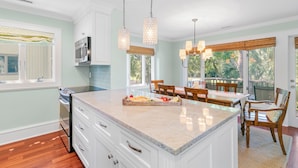A spacious kitchen with a large island, white cabinetry, and a dining area with wooden chairs. - Updated villa on golf course, 3 min to beach! (Kiawah Island)