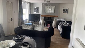 A living room with a black sofa, a coffee table with bowls, a fireplace with decorative vases, and a television. - Immaculate 3-bed House in Bridgnorth (Bridgnorth)