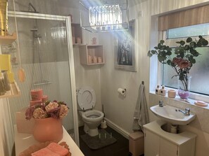 A bathroom with a shower, toilet, sink, and a window with a plant. - Immaculate 3-bed House in Bridgnorth (Bridgnorth)