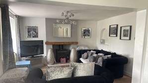 A living room with a black sofa, a television, a fireplace, and framed pictures on the wall. - Immaculate 3-bed House in Bridgnorth (Bridgnorth)