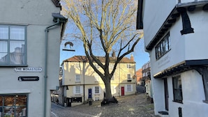 Una calle empedrada con edificios, incluyendo 'The Monastery' y 'Britons Arms'.