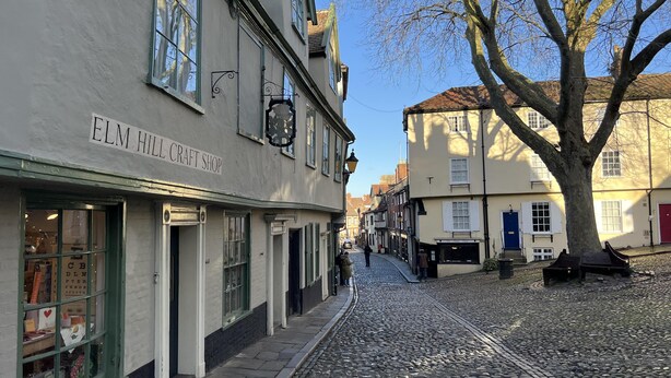 Una calle adoquinada con un edificio que dice 'ELM HILL CRAFT SHOP'.