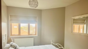 Un dormitorio con cama, radiador, ventana con vista a edificios y lámpara colgante.
