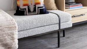 En moderne stue med en grå sofa, en beige pude, en dekorativ pude og en stor vævet vase på et træsidebord.