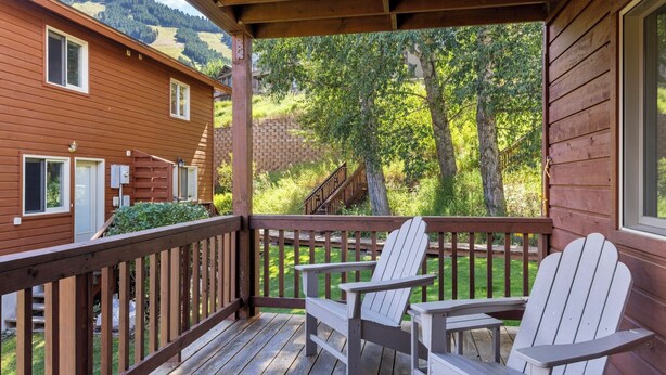 En træterrasse med to Adirondack-stole og en murstensvæg i baggrunden.