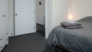 A bedroom with a bed, a nightstand, a lamp, and a door leading to another room. - Prospectors Inn (Kirkland Lake)