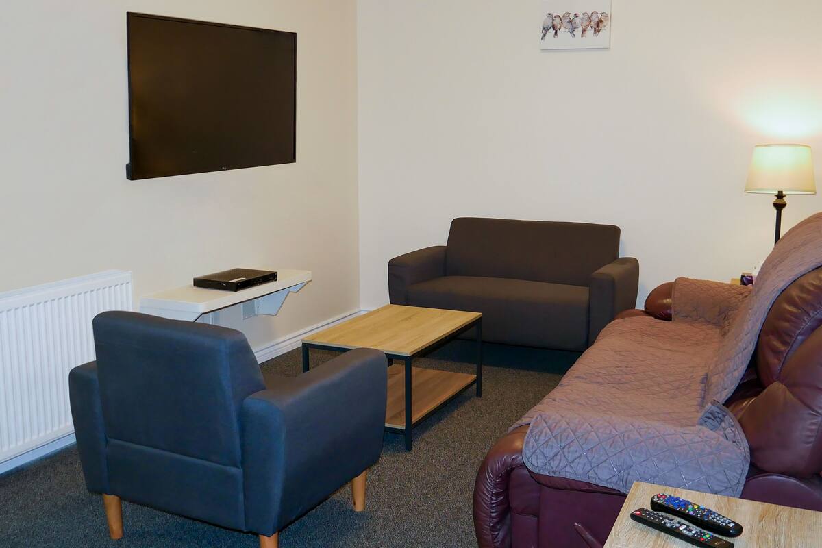 Un salon comprenant un canapé, un fauteuil, une table basse et un téléviseur à écran plat fixé au mur.