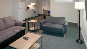 A compact living space with a sofa, armchair, coffee table, and a small kitchen area. - Prospectors Inn (Kirkland Lake)