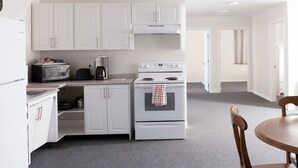 A compact kitchen with white cabinets, a microwave, a coffee maker, and a stove. - Prospectors Inn (Kirkland Lake)
