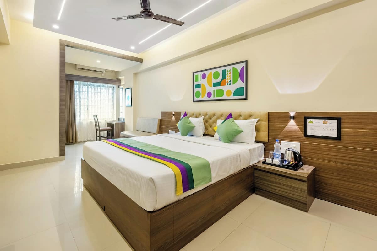 A modern hotel room with a large bed, a wooden headboard, a bedside table with a lamp, and a ceiling fan.