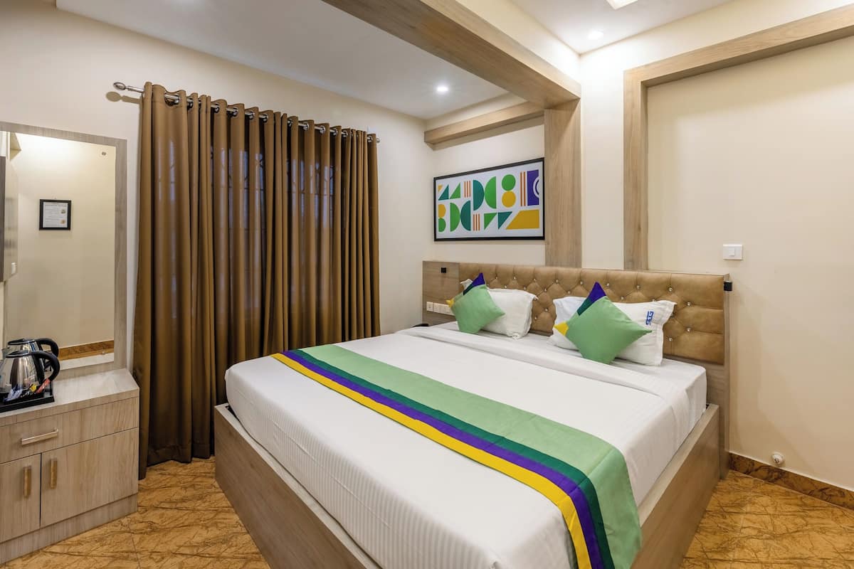 A hotel room with a bed, a nightstand, a coffee maker, and a curtain.