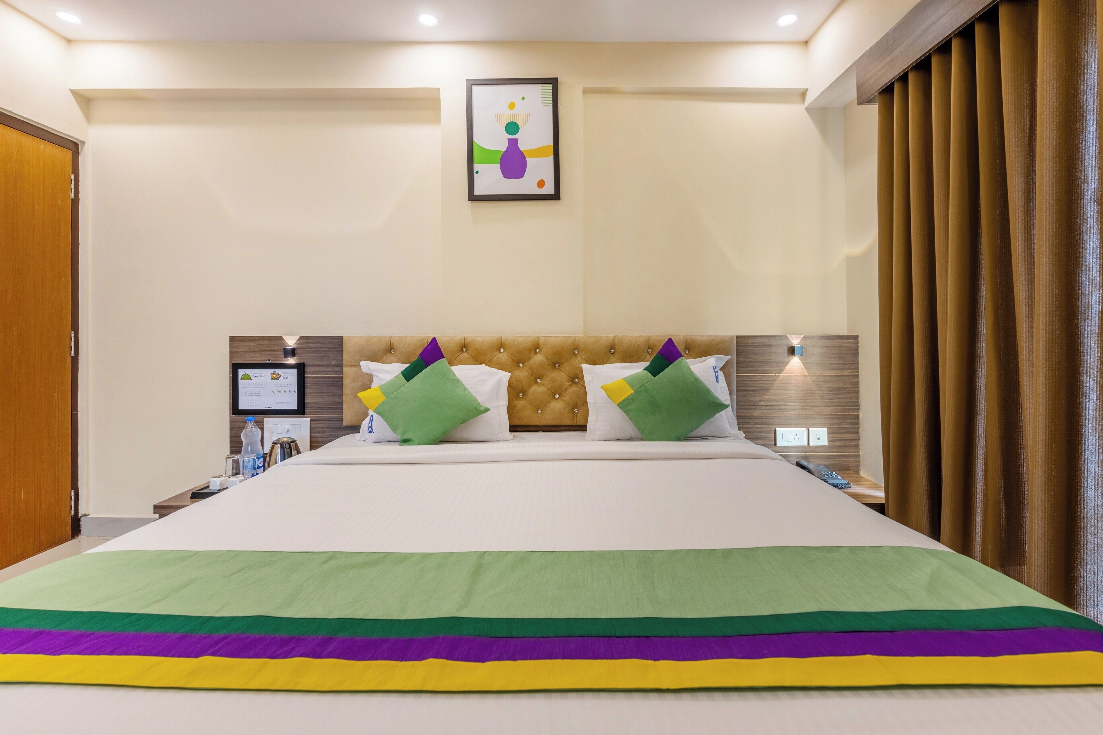 Una habitación de hotel con una cama grande, un televisor en la pared y una obra de arte enmarcada sobre la cama.