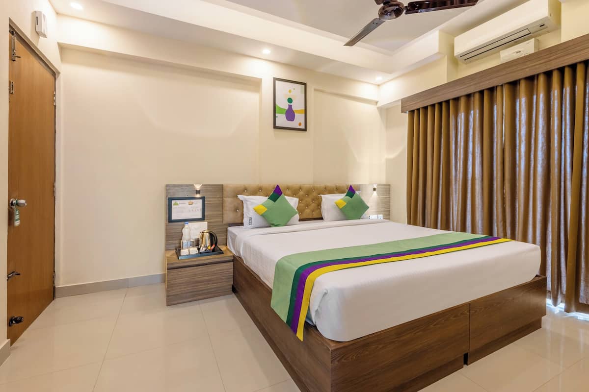A hotel room with a wooden bed, a nightstand with a lamp, a framed picture on the wall, and a window with curtains.