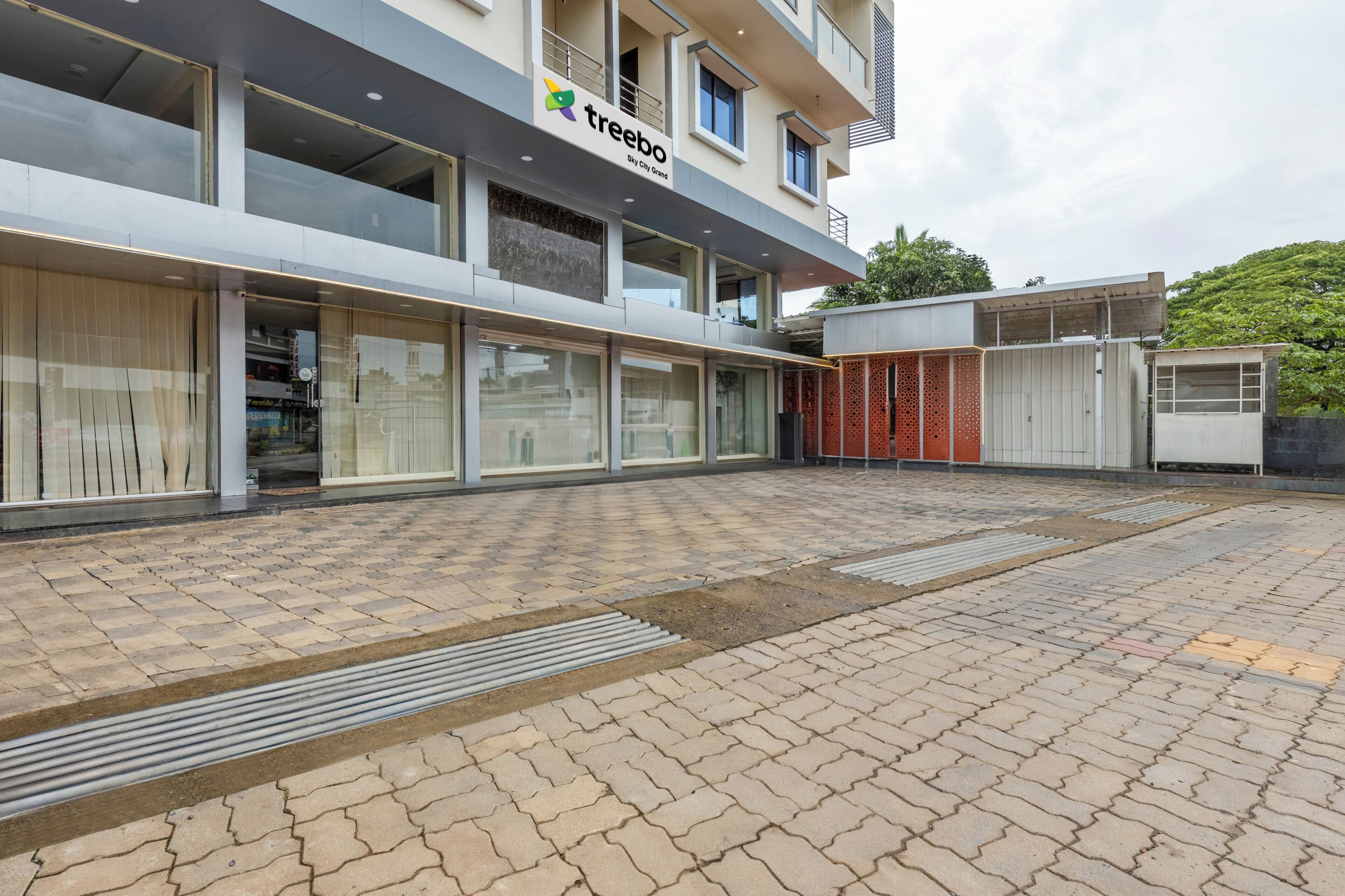 Ein modernes Gebäude mit einem 'treebo' Schild, großen Fenstern und einem gepflasterten Innenhof.