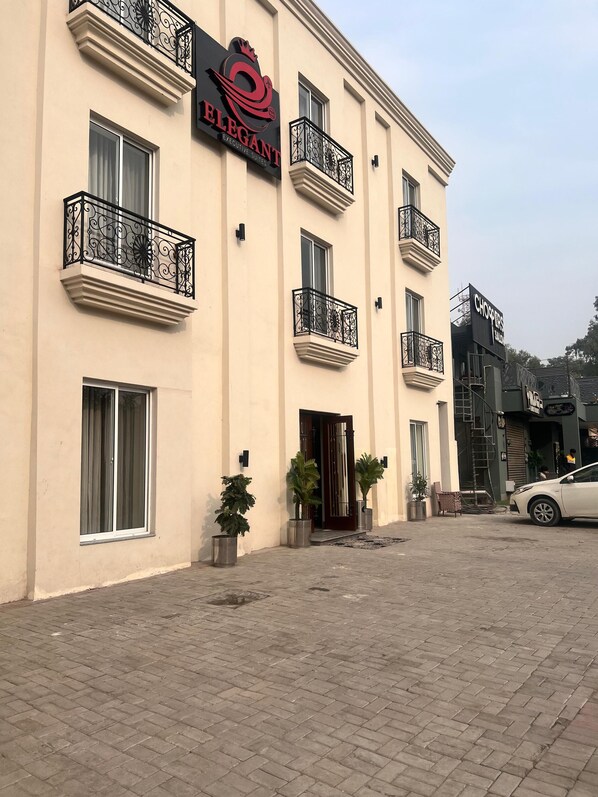 A building with balconies, a sign for 'ELEGANT Executive Suites,' and a parked car. - Hotel Elegant Executive Suites (Multan)