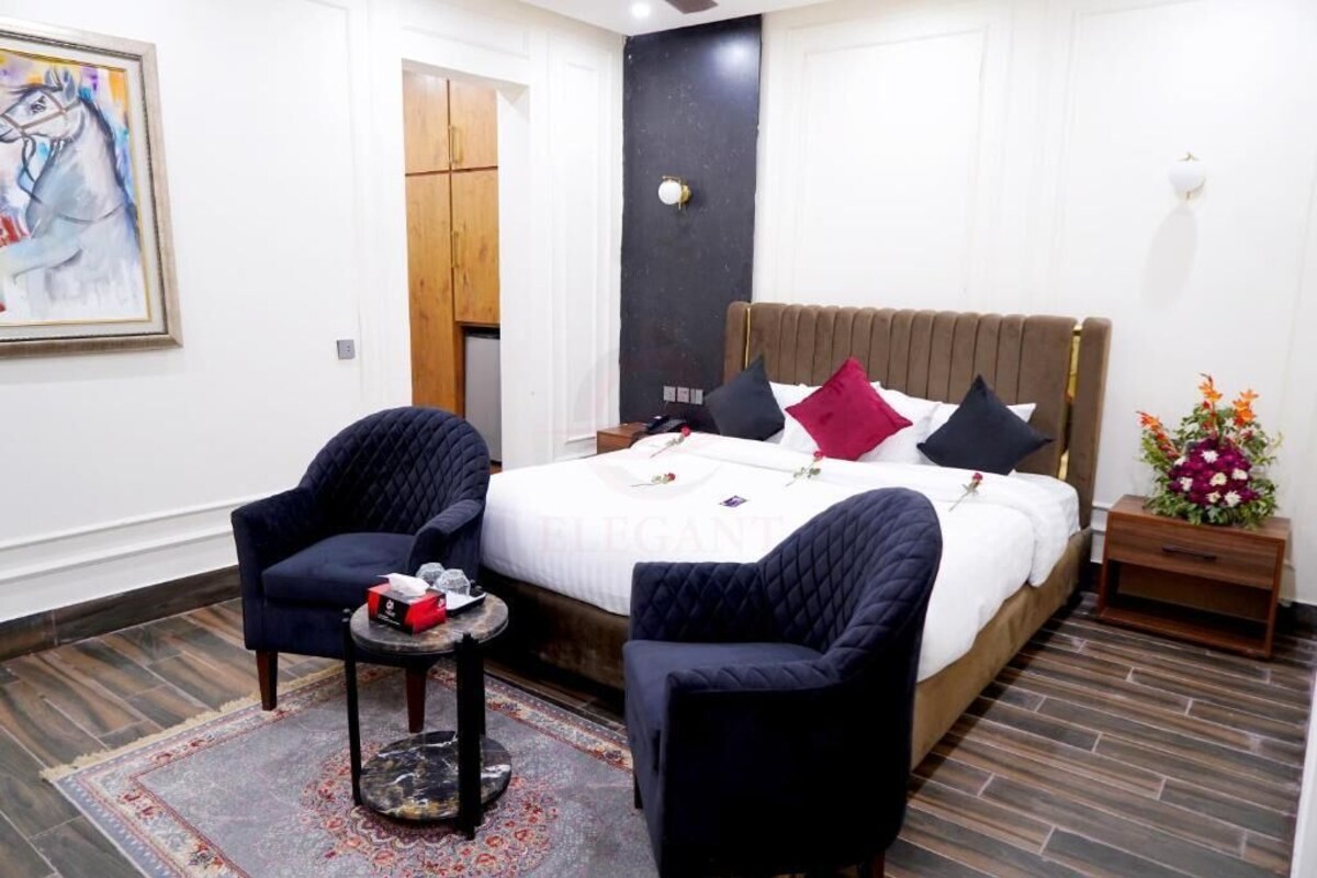 A modern hotel room with a large bed, two armchairs, a small table, and a decorative vase.